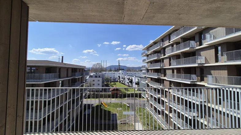 Geräumiger Balkon mit Fliesenboden und Blick auf die umliegenden Wohngebäude und Berge.