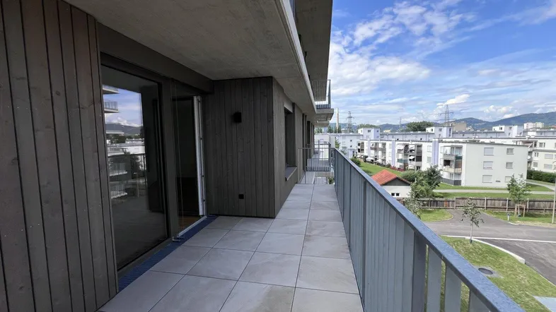 Langer, gefliester Balkon mit Holzverkleidung und Blick auf die umliegenden Gebäude und den Himmel.