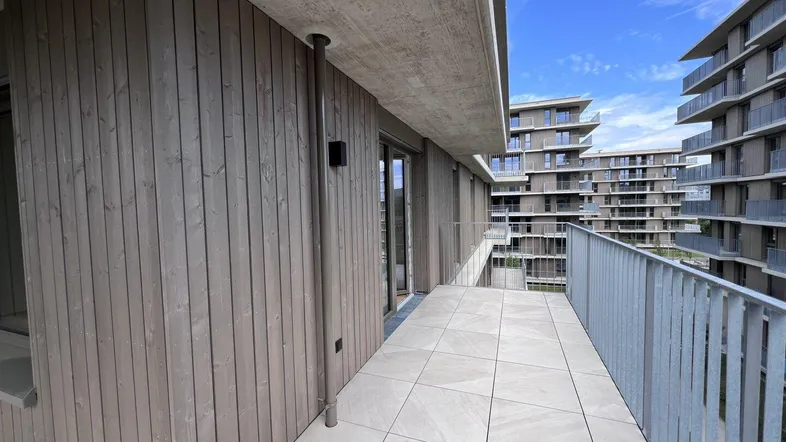 Geräumiger Balkon mit Fliesenboden und Blick auf die moderne Wohnanlage.