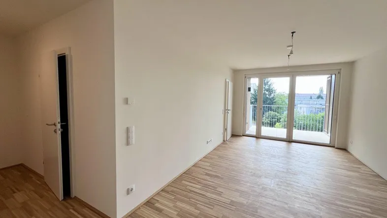 Helles, leeres Zimmer mit Parkettboden und Zugang zu einem Balkon, bereit zum Einrichten.