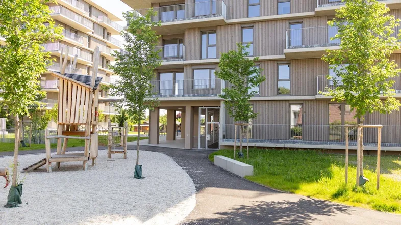 Moderner Wohnkomplex mit Holzfassade und Kinderspielplatz im Außenbereich.