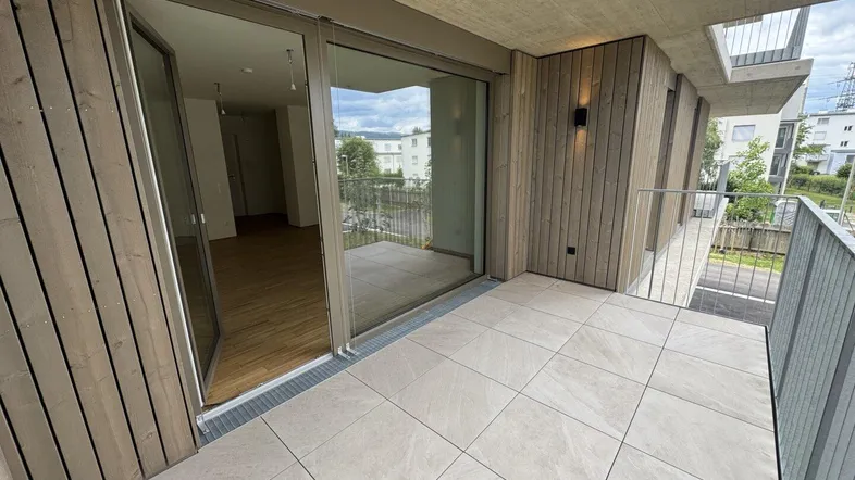 Balkon mit Fliesenboden und Holzverkleidung, bietet Zugang zum Innenbereich und Blick ins Grüne.