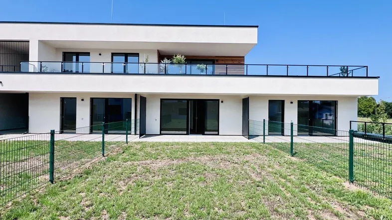 Moderne Wohnanlage mit weißer Fassade, großen Fenstern und Balkonen, umgeben von Grünflächen.
