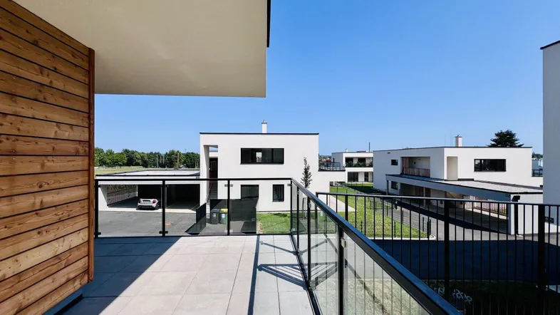 Moderner Balkon mit Glasgeländer und Blick auf die umliegenden Neubauten und Grünflächen.