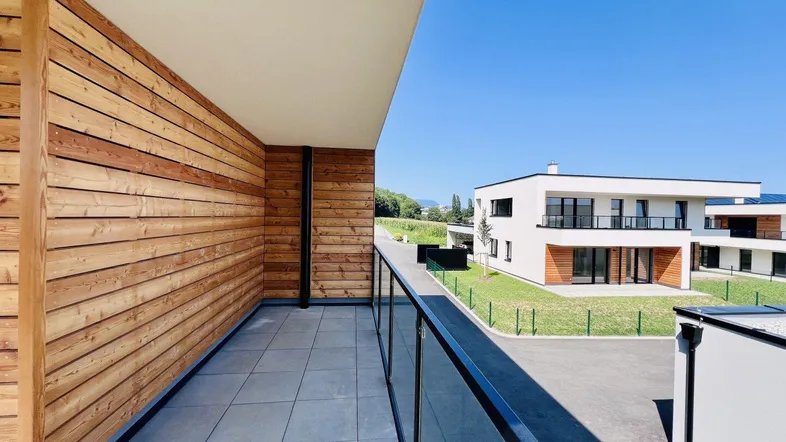 Moderner Balkon mit Holzverkleidung, Fliesenboden und Glasgeländer mit Blick auf die Umgebung.