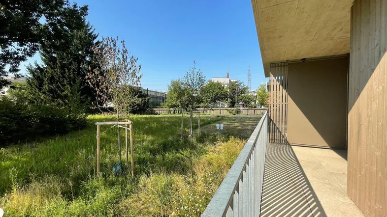 Heller Balkon mit Blick ins Grüne und auf die umliegende Natur unter blauem Himmel.