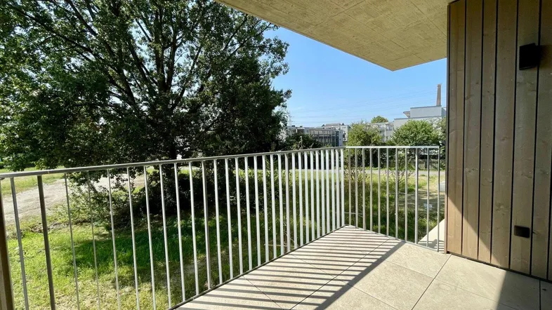 Heller Balkon mit Fliesenboden und Metallgeländer, bietet einen grünen Ausblick auf Bäume und Umgebung.