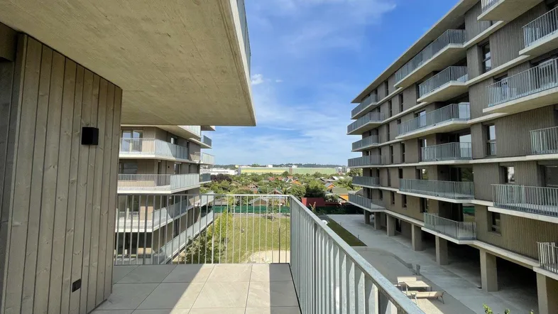 Geräumiger Balkon mit Fliesenboden und Blick auf moderne Wohngebäude und die umliegende Landschaft.