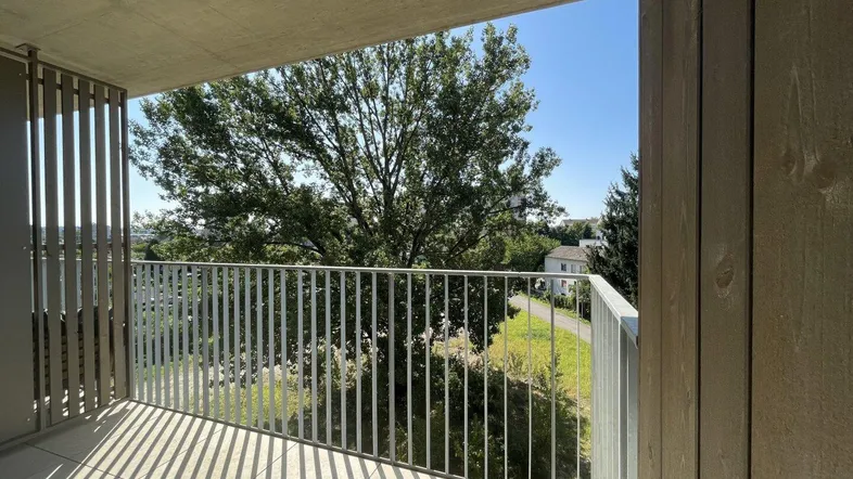 Geräumiger Balkon mit Fliesenboden, Metallgeländer und Blick ins Grüne unter blauem Himmel.