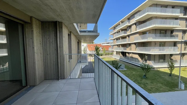 Geräumiger Balkon mit Fliesenboden und Blick auf die moderne Wohnanlage sowie Grünflächen.