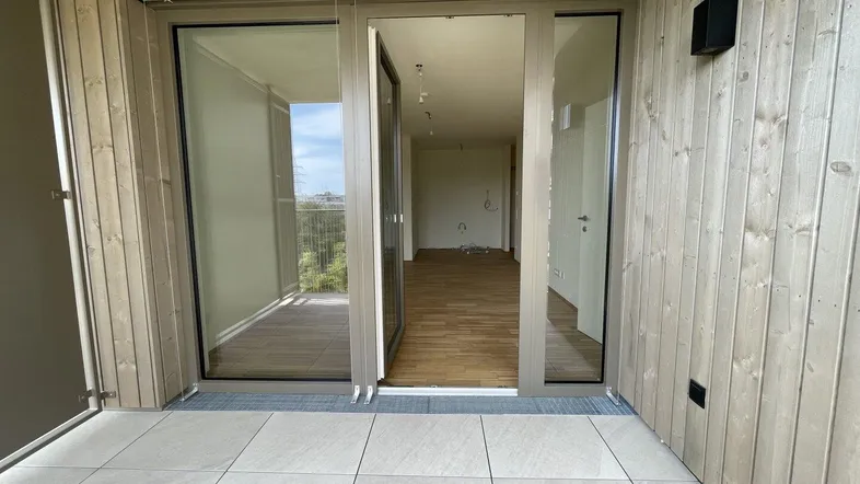 Geräumiger Balkon mit Fliesenboden und Holzverkleidung, der den Blick in den hellen Innenraum freigibt.