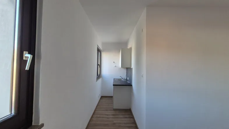 Schmaler Raum mit integrierter Küchenzeile, Laminatboden und Fenster für natürliches Licht.