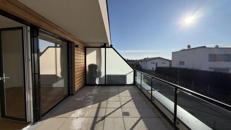 Sonniger Balkon mit Fliesenboden, Glasgeländer und Holzverkleidung, bietet Zugang zum Innenbereich.