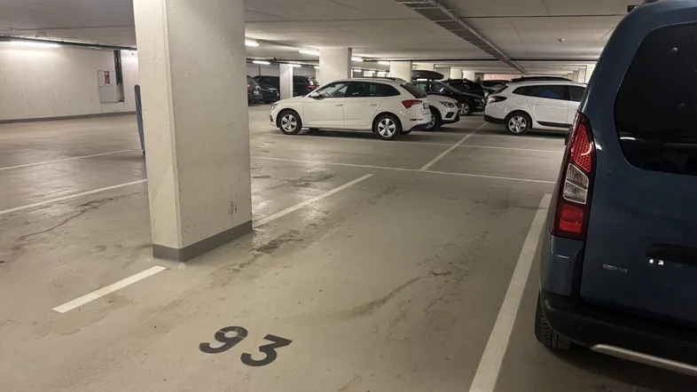 Tiefgarage mit markierten Stellplätzen und mehreren geparkten Fahrzeugen unter künstlicher Beleuchtung.