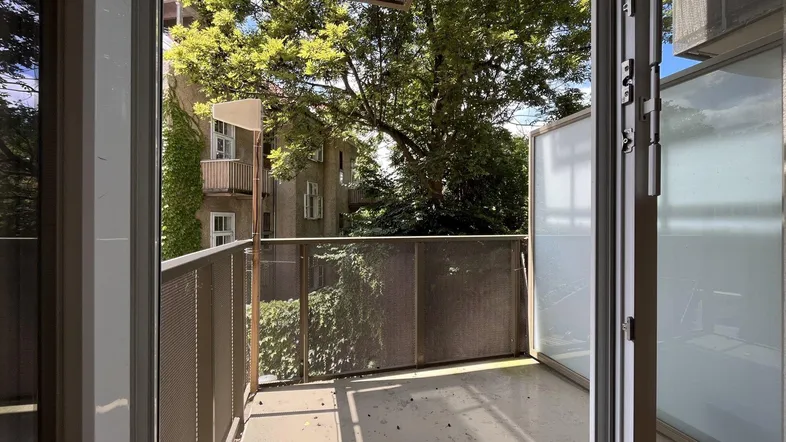 Heller Balkon mit Metallgeländer und Blick ins Grüne sowie auf umliegende Gebäude.