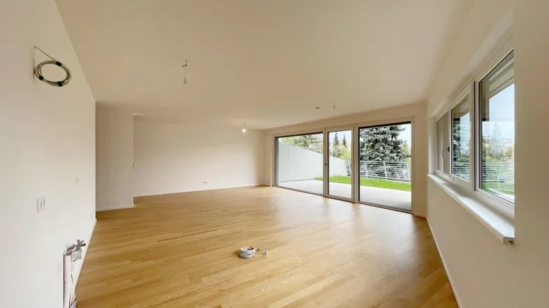 Helles, leeres Wohnzimmer mit großen Schiebetüren zum Garten und Holzparkettboden.