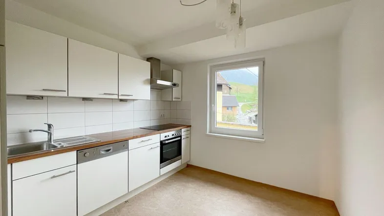 Funktionale Küche mit weißen Schränken, Holz-Arbeitsplatte und Fenster mit Blick ins Grüne.