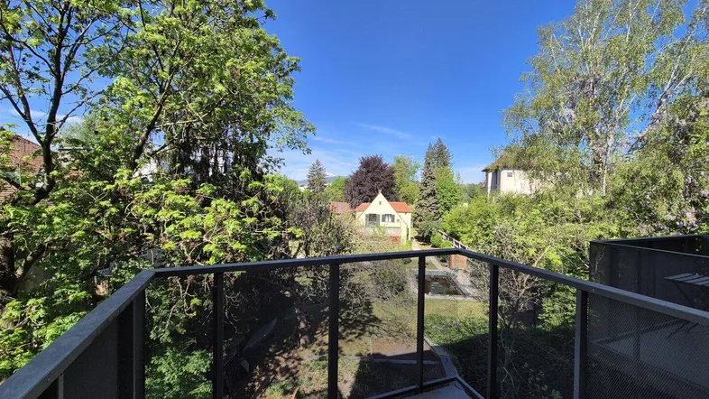 Balkon mit Metallgeländer und weitem Blick ins Grüne und auf umliegende Häuser.