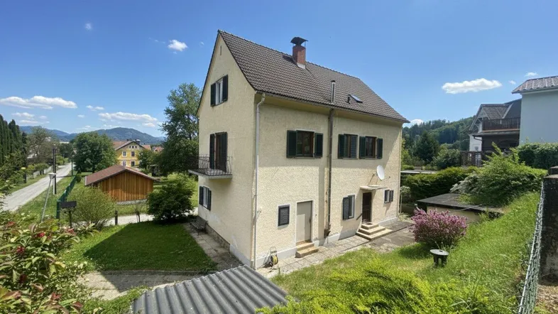 Freistehendes Haus mit Satteldach, Balkon und Garten in ländlicher Umgebung mit Bergblick.
