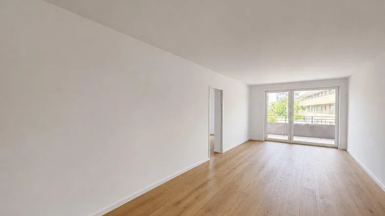 Helles, leeres Zimmer mit Holzboden und Zugang zu einem Balkon, bereit zur Einrichtung.