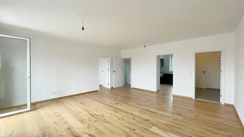 Geräumiges, helles Wohnzimmer mit neuem Holzboden und Zugang zu weiteren Räumen.