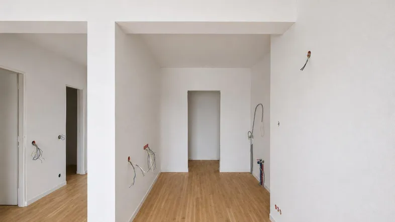 Unfertige Küche mit Holzboden und vorbereiteten Anschlüssen für die Kücheninstallation.