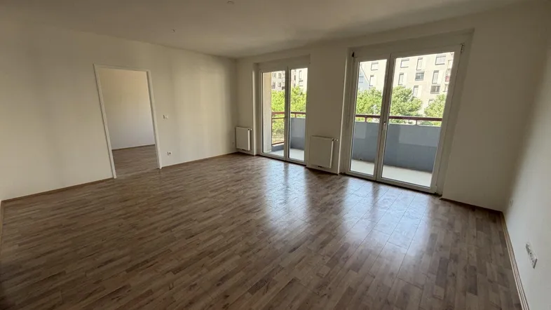 Helles Wohnzimmer mit Laminatboden und Zugang zu einem Balkon, bereit für die Einrichtung.