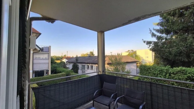 Möblierter Balkon mit Blick auf die grüne Umgebung und angrenzende Häuser.