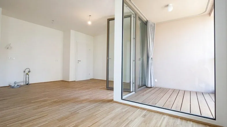 Heller, leerer Raum mit Parkettboden und Zugang zu einem Balkon, ideal für ein Wohnzimmer.