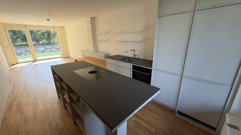 Heller offener Wohn- und Essbereich mit moderner Einbauküche, Kochinsel und Zugang zum Garten.