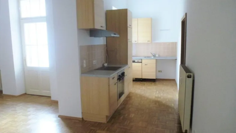 Helle Küche mit Holzparkettboden, Einbauschränken und Zugang zu einem Balkon oder einer Terrasse.