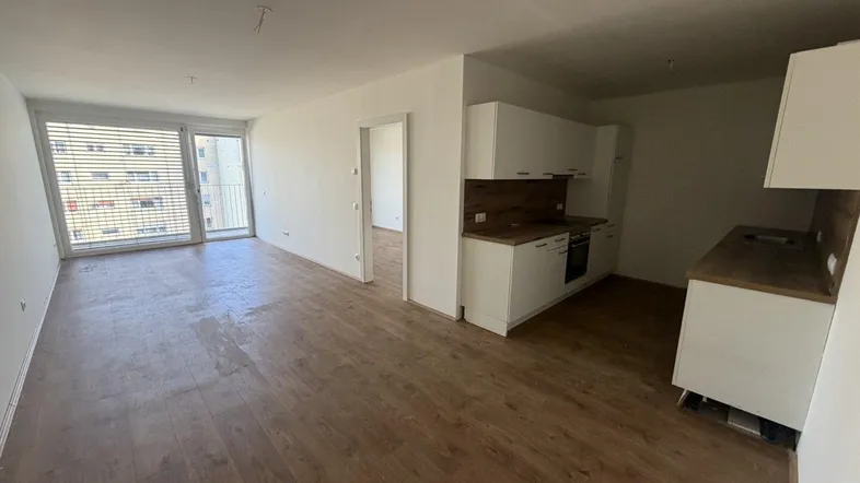 Heller offener Wohn- und Küchenbereich mit Holzboden und Zugang zum Balkon.