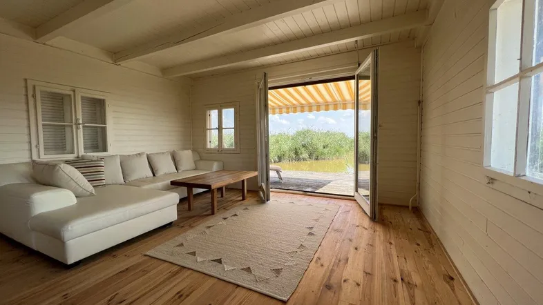 Helles Wohnzimmer mit Holzboden, weiß getäfelten Wänden und direktem Zugang zur Terrasse mit Seeblick.