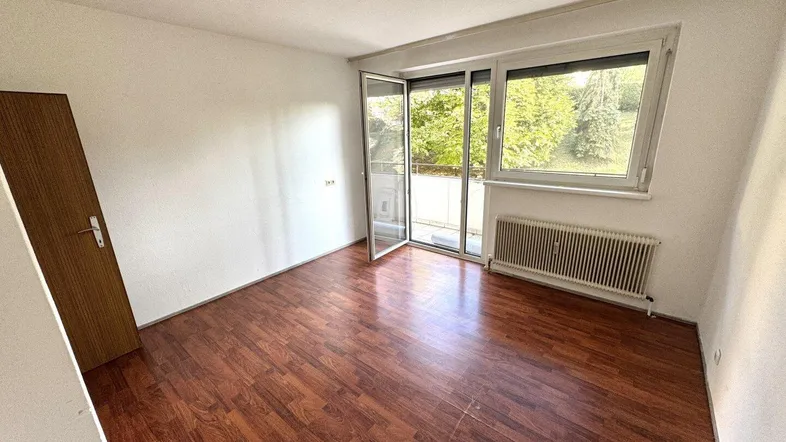 Helles Zimmer mit dunklem Laminatboden und Zugang zu einem Balkon, ideal als Wohn- oder Schlafzimmer.