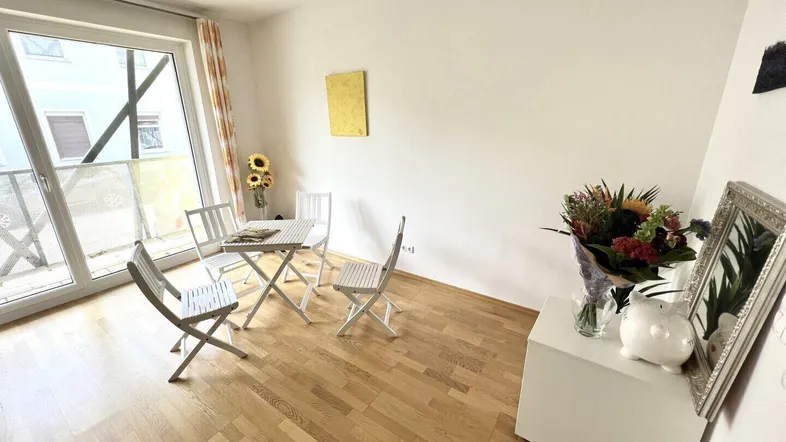Heller Wohnbereich mit Holzboden, Zugang zum Balkon und minimalistischer Einrichtung.