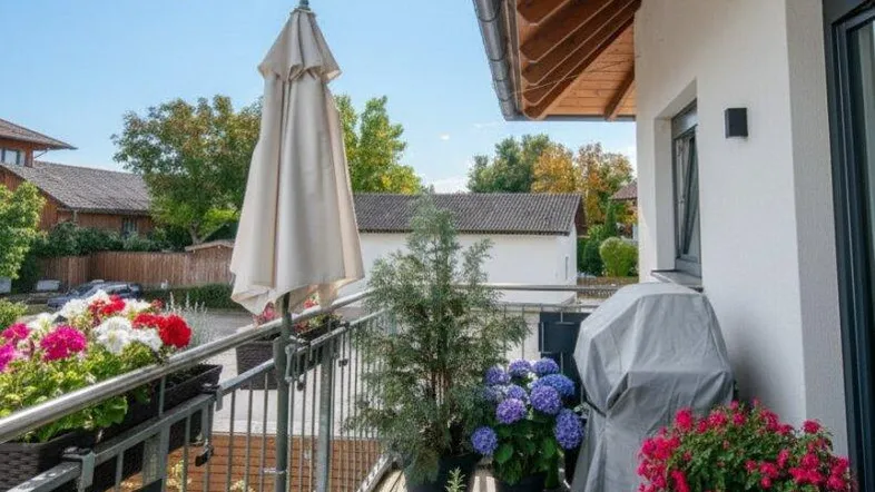 Sonniger Balkon mit Holzboden, Pflanzen, Grill und Sitzgelegenheiten für entspannte Stunden.