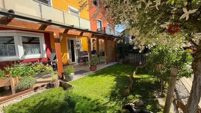 Gepflegter Gartenbereich mit Rasenfläche, überdachter Terrasse und Sitzgelegenheiten.