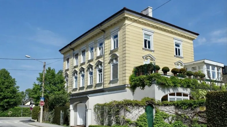 Traditionelles Mehrfamilienhaus mit gelber Fassade und gepflegter Außenanlage an einer ruhigen Straße.