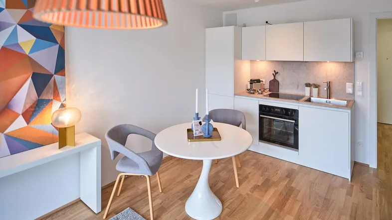 Moderner Wohnbereich mit integrierter Küchenzeile, Esstisch und Parkettboden.