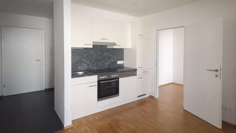 Moderne Einbauküche mit weißen Schränken, dunkler Arbeitsplatte und Holzfußboden in einem offenen Bereich.