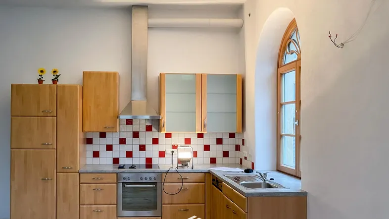 Helle Küche mit Holzschränken, rot-weiß gefliestem Fliesenspiegel und Bogenfenster.