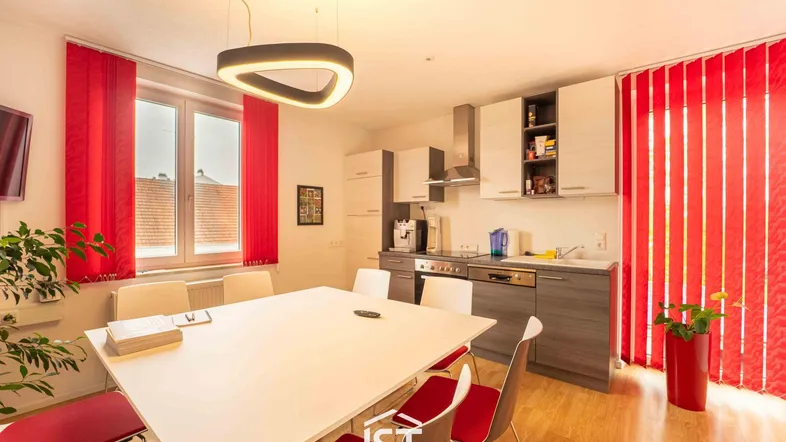 Helle, moderne Küche mit Essbereich, ausgestattet mit Einbauschränken und einem großen Esstisch, beleuchtet von einer Designerlampe.