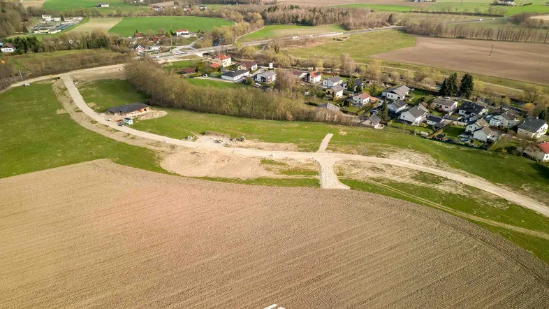 Luftaufnahme eines ländlichen Baugebiets mit Feldern, Wiesen und einigen Häusern in der Ferne.