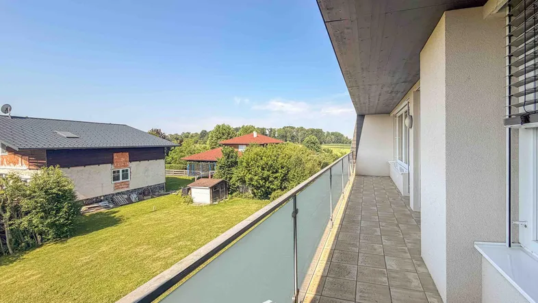 Langer Balkon mit Fliesenboden und Glasgeländer, bietet einen schönen Blick ins Grüne.