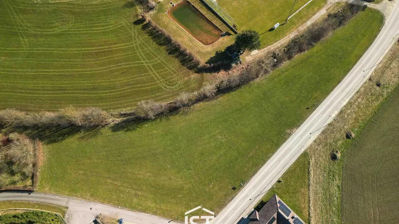 Luftaufnahme eines großen grünen Grundstücks mit angrenzender Straße und Sportanlage.