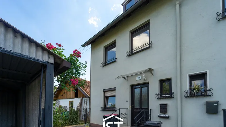 Vorderansicht eines Wohnhauses mit Eingangsbereich, Fenstern und einer angrenzenden Garage.