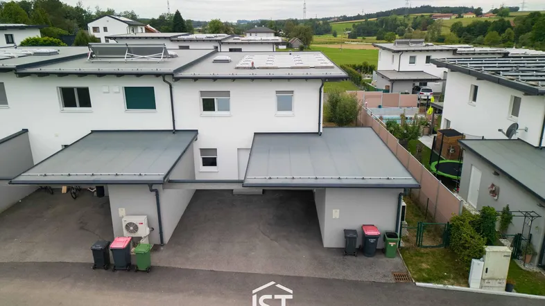 Moderne Reihenhäuser mit Carports und Photovoltaikanlagen in ländlicher Umgebung.