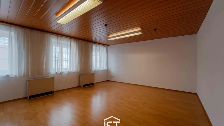 Geräumiger leerer Raum mit Holzdecke, Parkettboden und mehreren Fenstern, die Tageslicht hereinlassen.