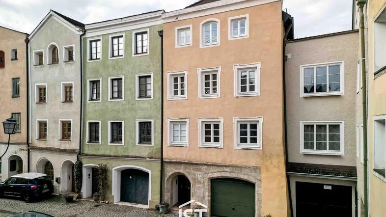 Historische Gebäudezeile mit farbigen Fassaden und Garagenzugängen in einer gepflasterten Gasse.
