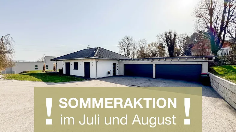 Modernes weißes Haus mit dunklem Satteldach und einer Doppelgarage, umgeben von gepflegten Grünflächen und einer Auffahrt.